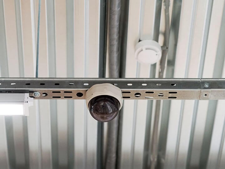 Security camera and smoke detector hanging on a metal interior ceiling